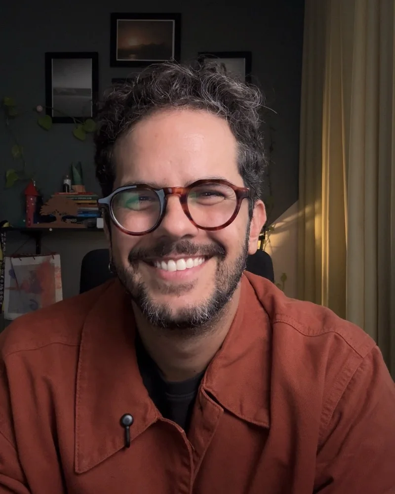 Edu Esperidião sorrindo, de jaqueta laranja, no escritório onde grava seus vídeos.